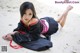 A woman in a black and red dress laying on the sand.