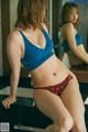 A woman in a blue bra and red panties standing in front of a mirror.