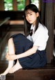 A young woman sitting on a wooden bench in a school uniform.