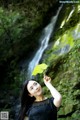 A woman holding a leaf in front of a waterfall.