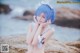 A woman with blue hair is posing on a rock by the ocean.