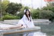 A woman in a white dress sitting on the edge of a pool.